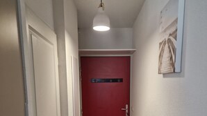 Ein schmaler Flur mit einer roten Tür am Ende, einer Lampe darüber und einem gerahmten Bild an der Wand.
