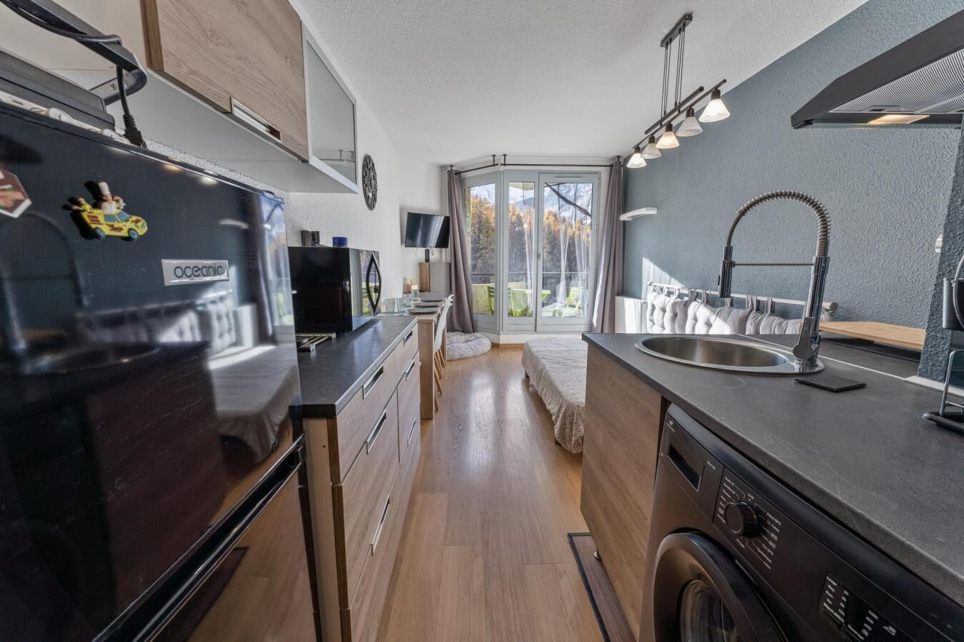 A modern kitchen with a built-in washing machine, a sink, and a large window overlooking a balcony.