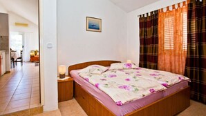 Un dormitorio con una cama de madera, una mesita de noche, una lámpara de noche, un cuadro enmarcado en la pared y una ventana con cortinas.