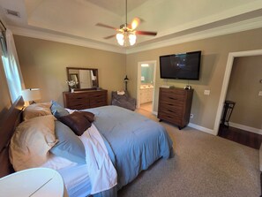 Ein Schlafzimmer mit einem großen Bett, einem Deckenventilator, einem Fernseher und einem durchgegangenen Tür sichtbaren Badezimmer.