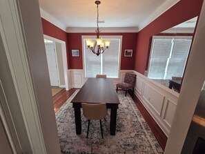 Comedor con una mesa larga, sillas, alfombra estampada y candelabro.
