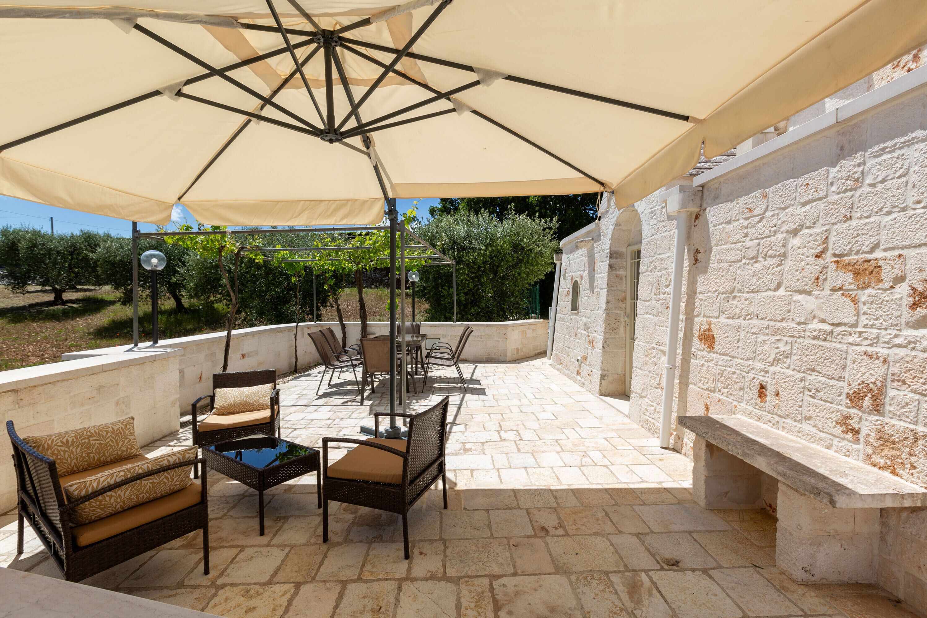 Eine Terrasse im Freien mit Tisch und Stühlen, einem großen Sonnenschirm und einer Steinmauer.
