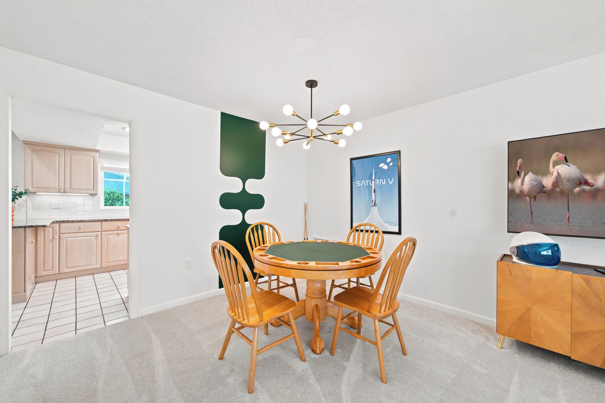 A dining area with a round table, wooden chairs, a chandelier, a painting, and a television on a wooden cabinet.