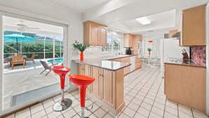 A spacious kitchen with wooden cabinets, a large island, and a view of a backyard patio. - Private House - Pool, Firepit, Dog Friendly, Walk to Beach, FREE EV Charger (Cocoa Beach)