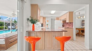 Een moderne keuken met houten kasten, een centraal eiland en twee oranje barkrukken.