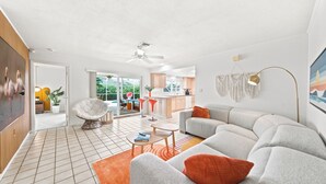 A modern living room with a sofa, armchair, and coffee table. There is a kitchen area in the background with a dining table and chairs. - Private House - Pool, Firepit, Dog Friendly, Walk to Beach, FREE EV Charger (Cocoa Beach)