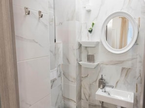 Ein Badezimmer mit Marmorfliesen, einem Waschbecken, einem Spiegel und einer kleinen Ablagefläche mit einer Pflanze.