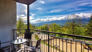 A balcony with a table and chairs, overlooking a mountainous landscape with trees and a clear sky.