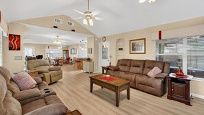 Ein geräumiges Wohnzimmer mit Ledersofas, einem Holztisch und Deckenventilatoren, im Hintergrund ein Essbereich.