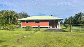 Un edificio de una sola planta con fachada roja y tejado verde, rodeado de césped cuidado y palmeras.