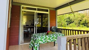 Un espacio exterior cubierto con una mesa y sillas, una puerta corredera de vidrio que da a un área interior y vistas a la vegetación.