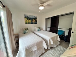 Une chambre d’hôtel avec deux lits, un ventilateur de plafond, un tableau et une vue sur l’extérieur.