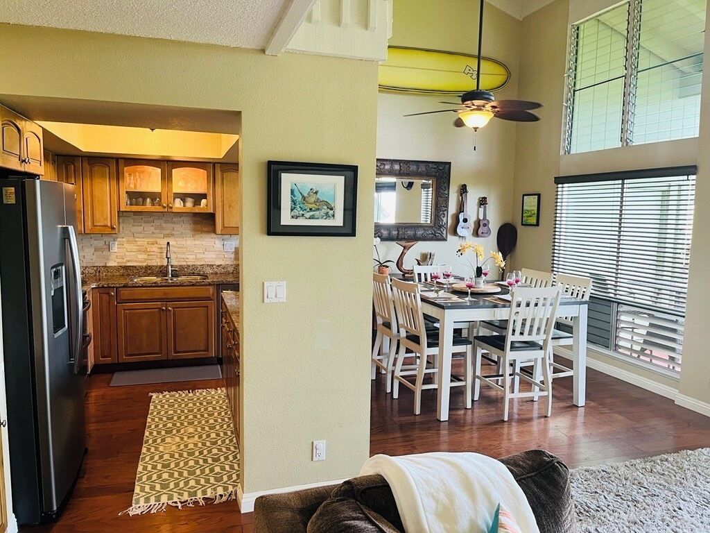 A kitchen with wooden cabinets, a dining area with white chairs, and a ceiling fan.