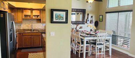 A kitchen with wooden cabinets, a dining area with white chairs, and a ceiling fan.