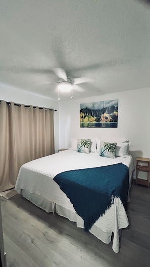 Ein Schlafzimmer mit einem großen Bett, einem Deckenventilator, einem Nachttisch und einem Bild an der Wand.