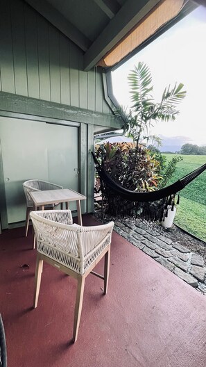 Eine überdachte Terrasse mit Korbmöbeln und einer Hängematte mit Blick auf eine Wiese.