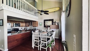 Une cuisine avec des meubles en bois, un coin repas avec des chaises blanches et un ventilateur de plafond.
