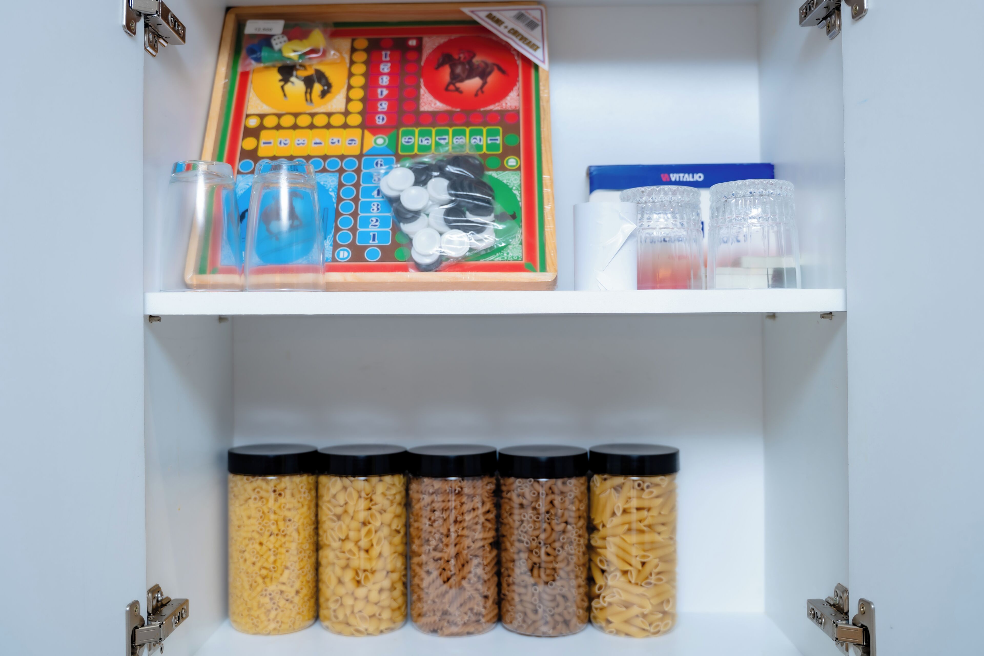 A storage unit with jars of pasta and a board game.