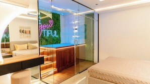 Une chambre d’hôtel moderne avec une cloison en verre, un banc en bois, un lit et un panneau lumineux au néon.