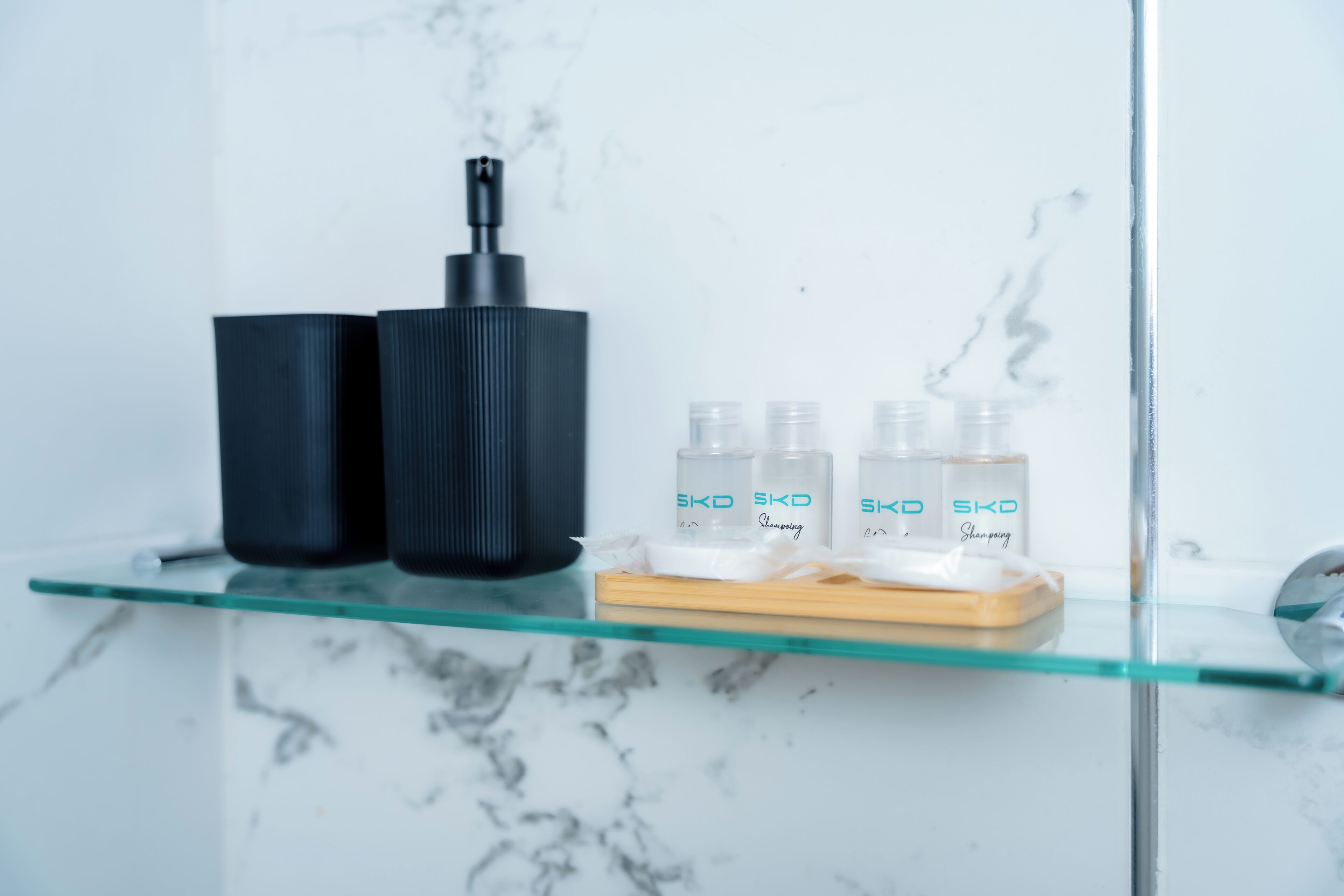 A bathroom with a glass shelf holding skincare products and a black bottle.