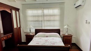 Un dormitorio con una cama de madera, dos mesitas de noche con lámparas, una ventana con persianas y un equipo de aire acondicionado en la pared.