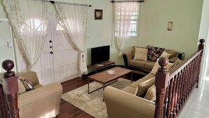 Una sala de estar con un conjunto de sofá, una mesa de centro, un televisor y una escalera con barandilla de madera.