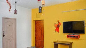Una habitación con puerta de madera, televisor montado en la pared y una pequeña mesa.