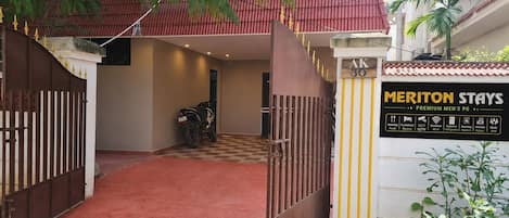 A gated entrance to Meriton Stays with a checkered floor, a motorcycle parked inside, and a signboard listing amenities.