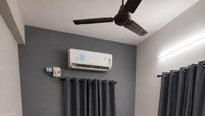 Una habitación con dos camas individuales, ventilador de techo, aire acondicionado y cortinas.