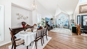 A dining area with a chandelier, wooden chairs, a white tablecloth, and a piano in the background.