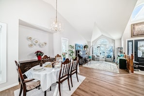 A dining area with a chandelier, wooden chairs, a white tablecloth, and a piano in the background.