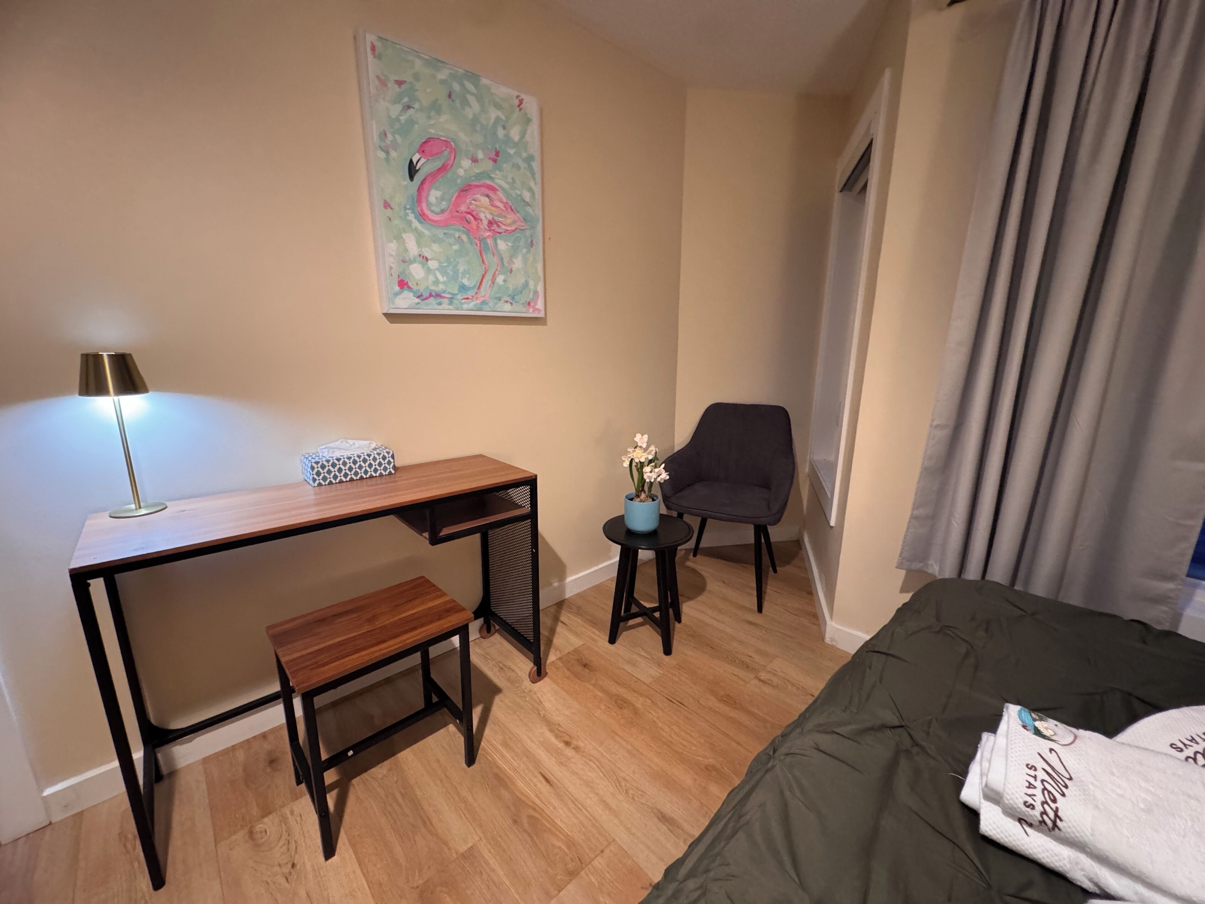 A hotel room with a desk, chair, bed, and a painting of a flamingo on the wall.