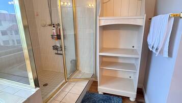 A bathroom with a glass-enclosed shower, a white vanity with shelves, and a blue rug.