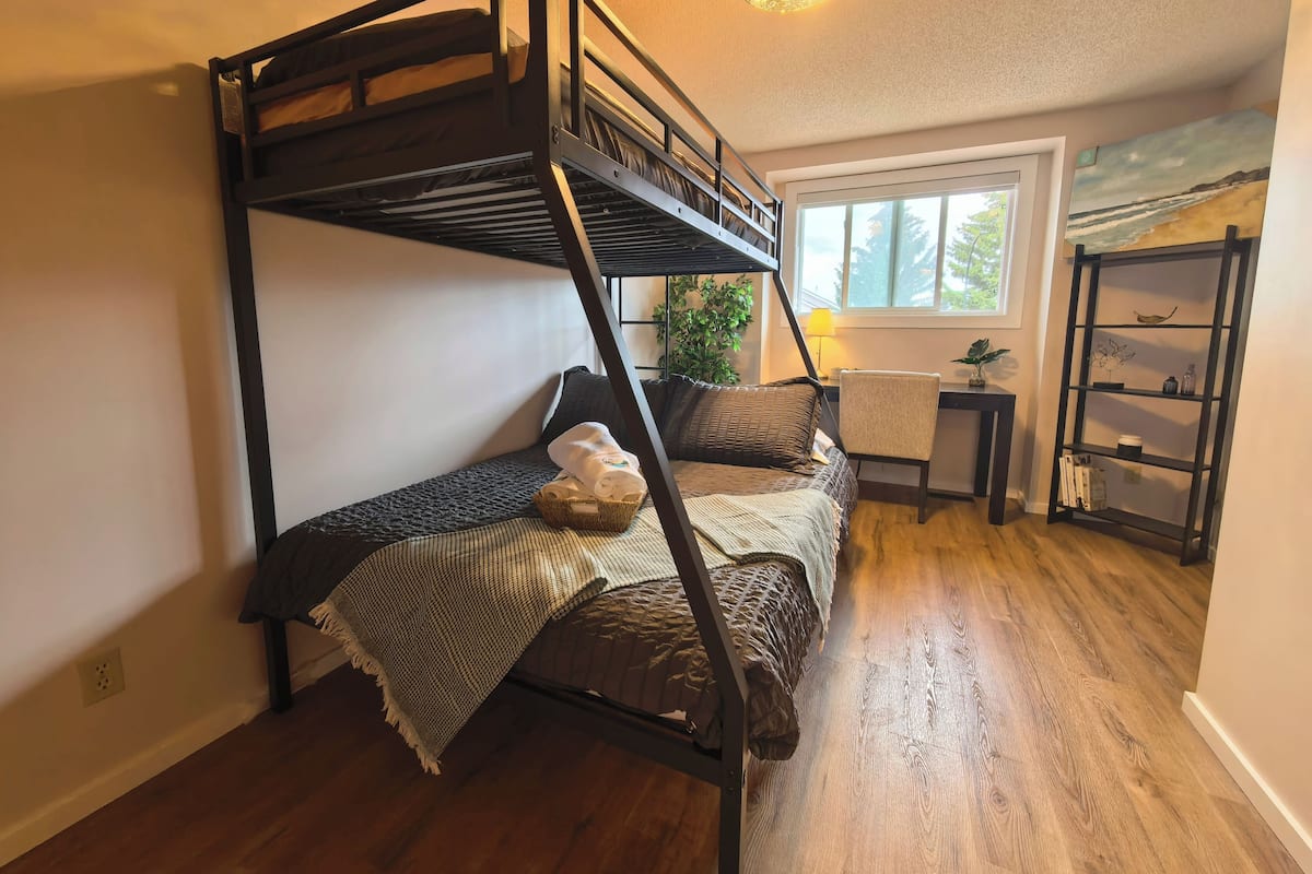 Una cama litera con escritorio y silla, una estantería y una ventana con vistas.