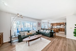 A spacious living room with a sofa, coffee table, and a view of the kitchen. - Metta Stays Edgemont (Calgary)