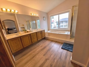 Ein Badezimmer mit Holzausstattung, einem großen Spiegel, einer Badewanne und einem Fenster mit Blick auf Gebäude.
