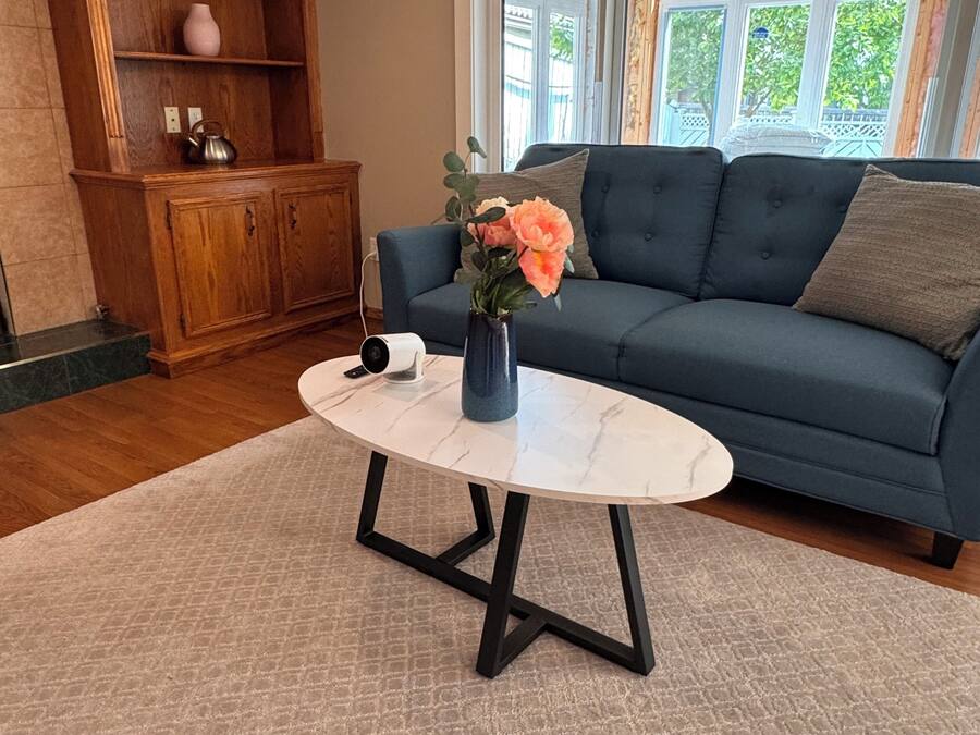Una sala de estar con un sofá azul, un aparador de madera, una mesa de centro de mármol y un florero con flores.