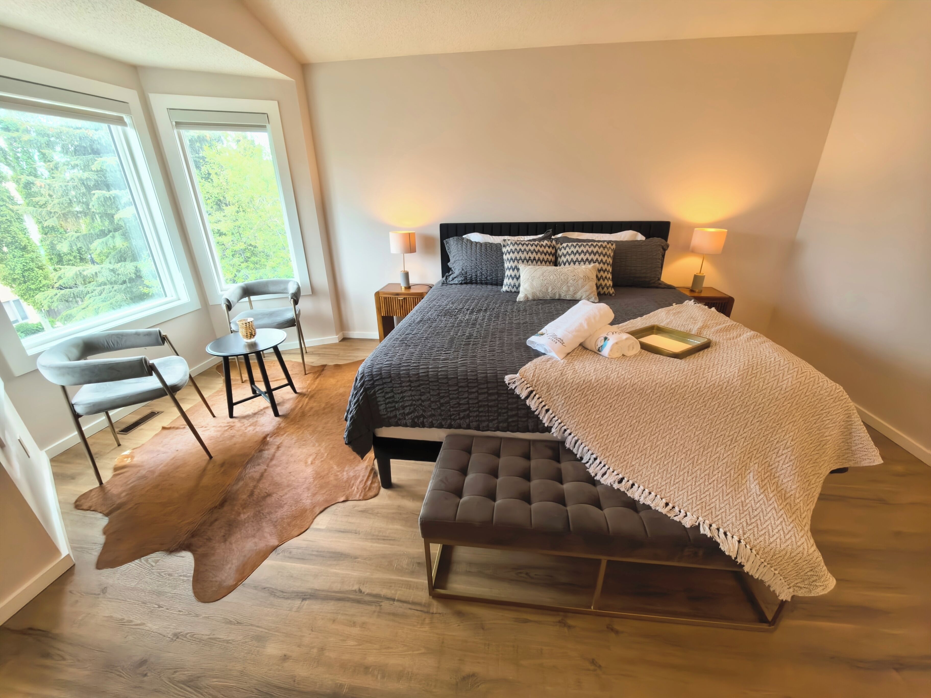 Ein Schlafzimmer mit einem großen Bett, zwei Nachttischlampen, einem Sessel, einem kleinen Tisch und einem Teppich.