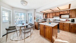 A modern kitchen with wooden cabinets, a central island, and a dining area with chairs.
