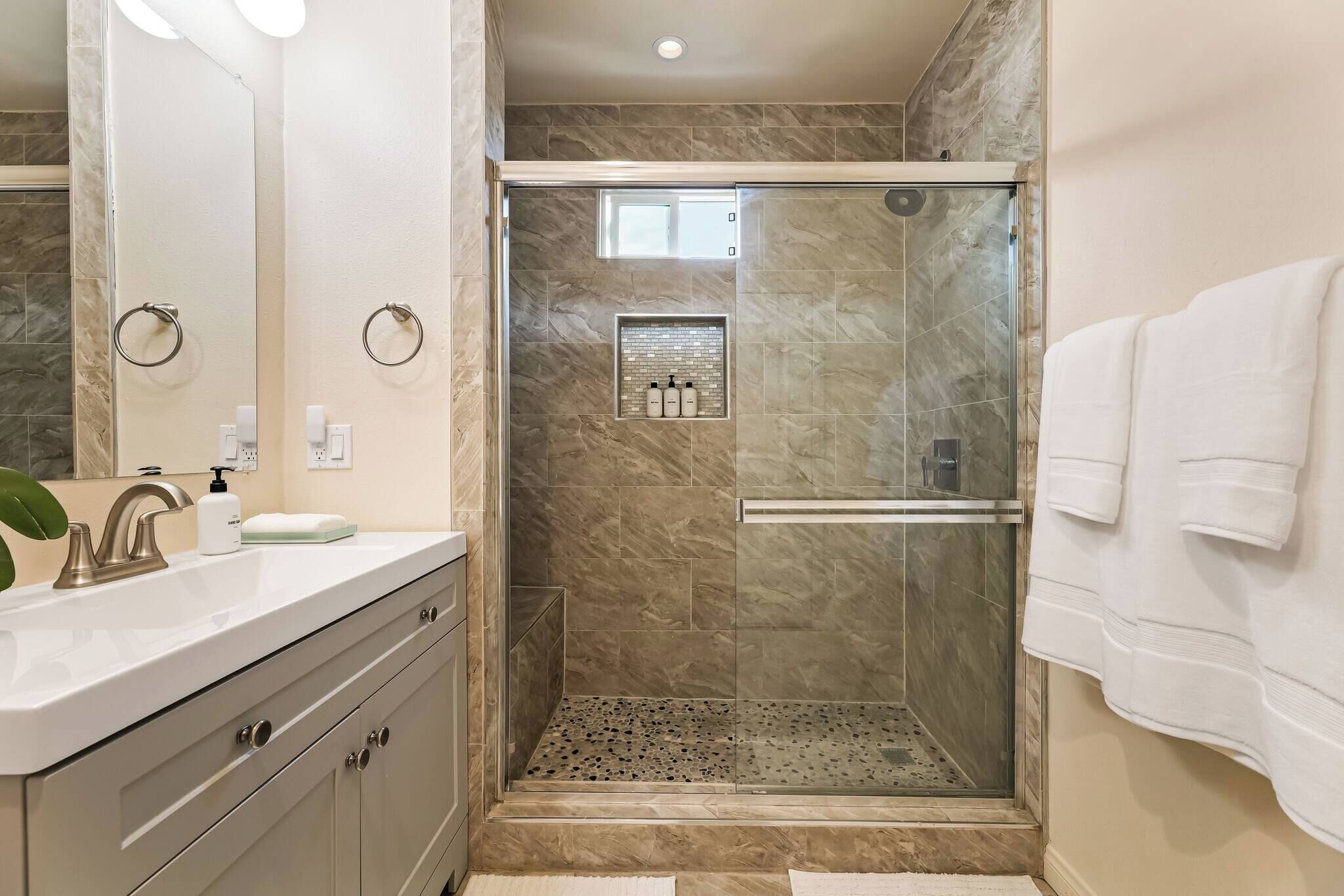 A modern bathroom with a glass-enclosed shower, a vanity with a mirror, and a towel rack.