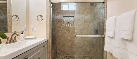 A modern bathroom with a glass-enclosed shower, a vanity with a mirror, and a towel rack.