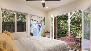 A bedroom with a bed, a ceiling fan, a large window, and a sliding glass door leading to an outdoor patio.