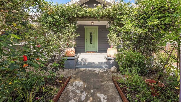 A house with a green door, a small porch, and a garden with potted plants.