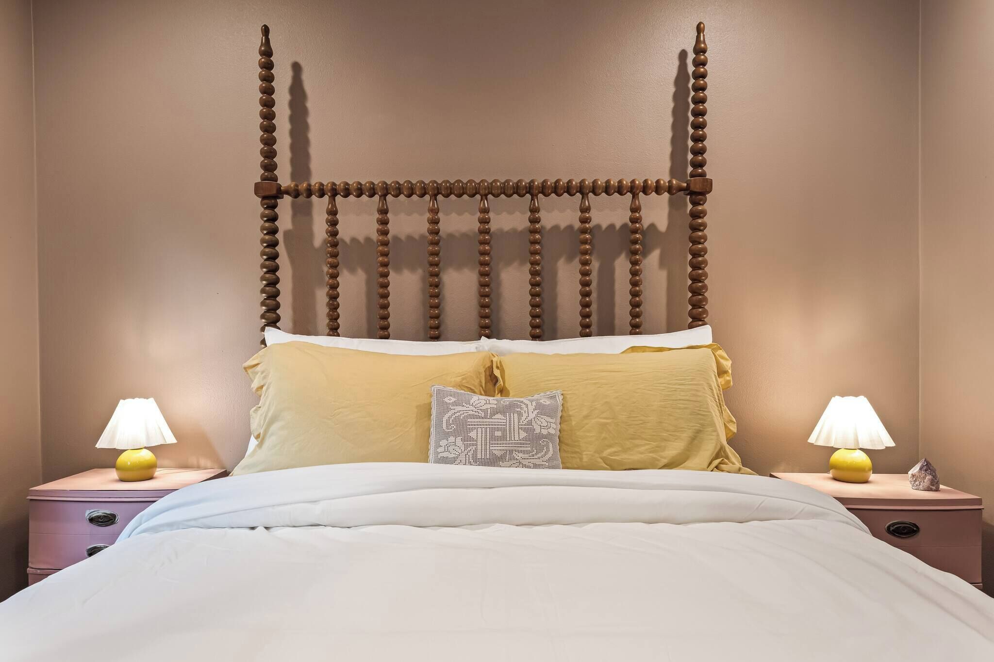 Un lit avec une tête de lit en bois, deux tables de chevet avec des lampes et un coussin à motifs.