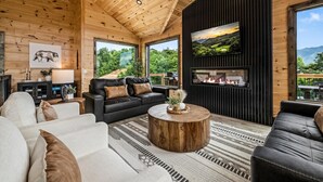 A modern log cabin interior with a fireplace, leather sofas, and a large TV screen. - Epic Views•HotTub•Theater•Near DT•Pool (Gatlinburg)