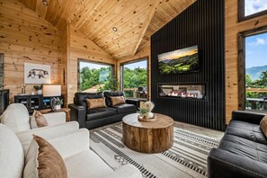 Ein modernes Blockhaus-Interieur mit Kamin, Ledersofas und einem großen Fernsehbildschirm.