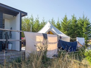 A tent with a peaked roof, a wooden deck, and a house with an open door. - 4 Person Holiday Home in Sejero (Sejero)
