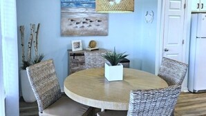 Ein Essbereich mit Korbstühlen, einem runden Holztisch, einer Hängeleuchte und einem Strandbild an der Wand.