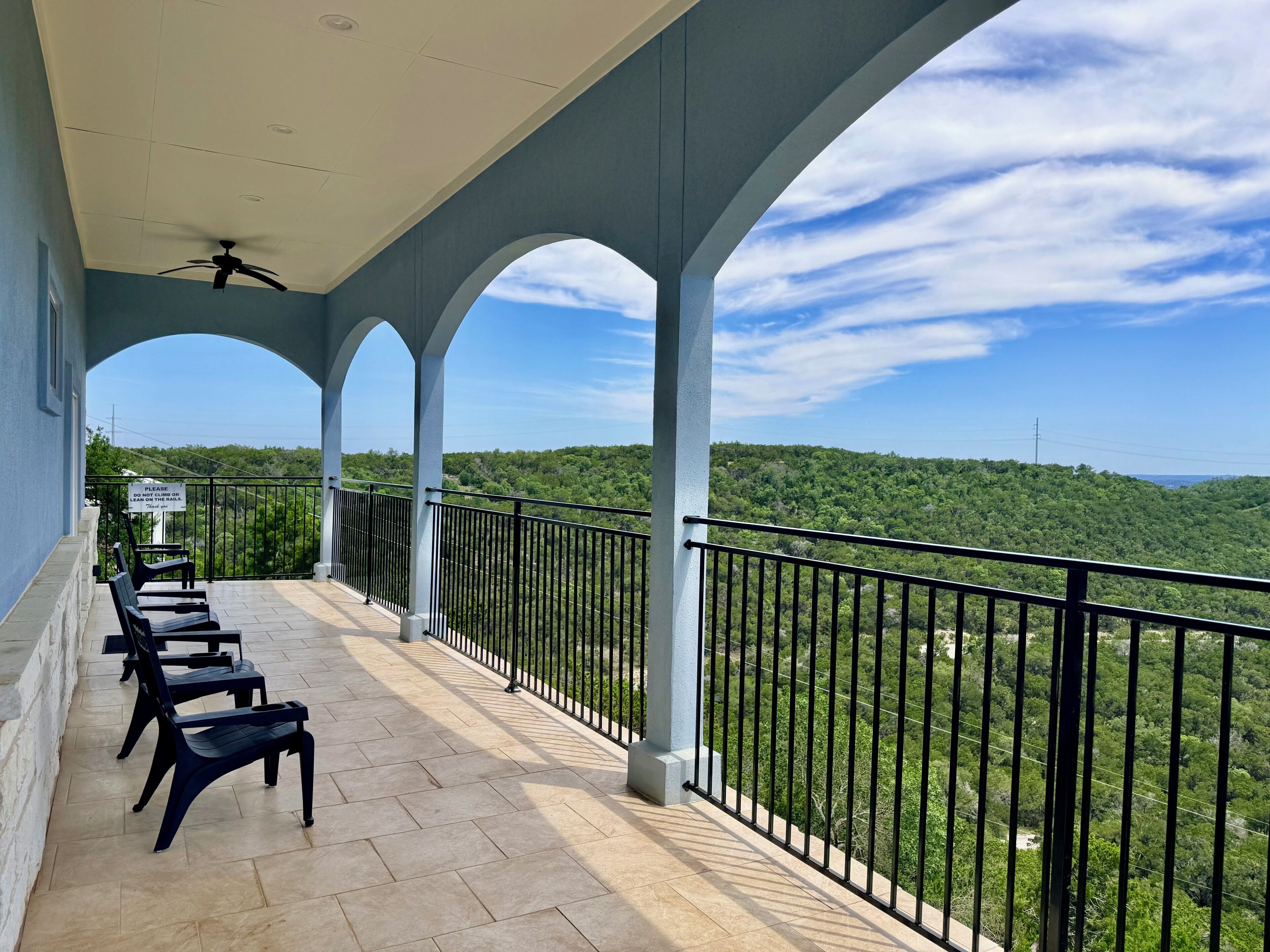 A balcony with a view of a forested landscape, a ceiling fan, and a sign on the railing.