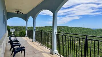 A balcony with a view of a forested landscape, a ceiling fan, and a sign on the railing.